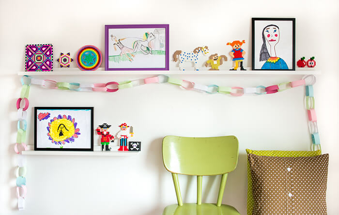 Elegantné biele obrazové police ozdobené farebnými detskými obrazmi a inými peknosťami Biela lišta v detskej izbe